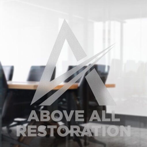 Cánh cửa kính mờ cát với logo hình học chữ A và dòng chữ "Above All Restoration" in đậm, thể hiện một phòng họp hiện đại và ghế văn phòng phía sau decal dán kính văn phòng.