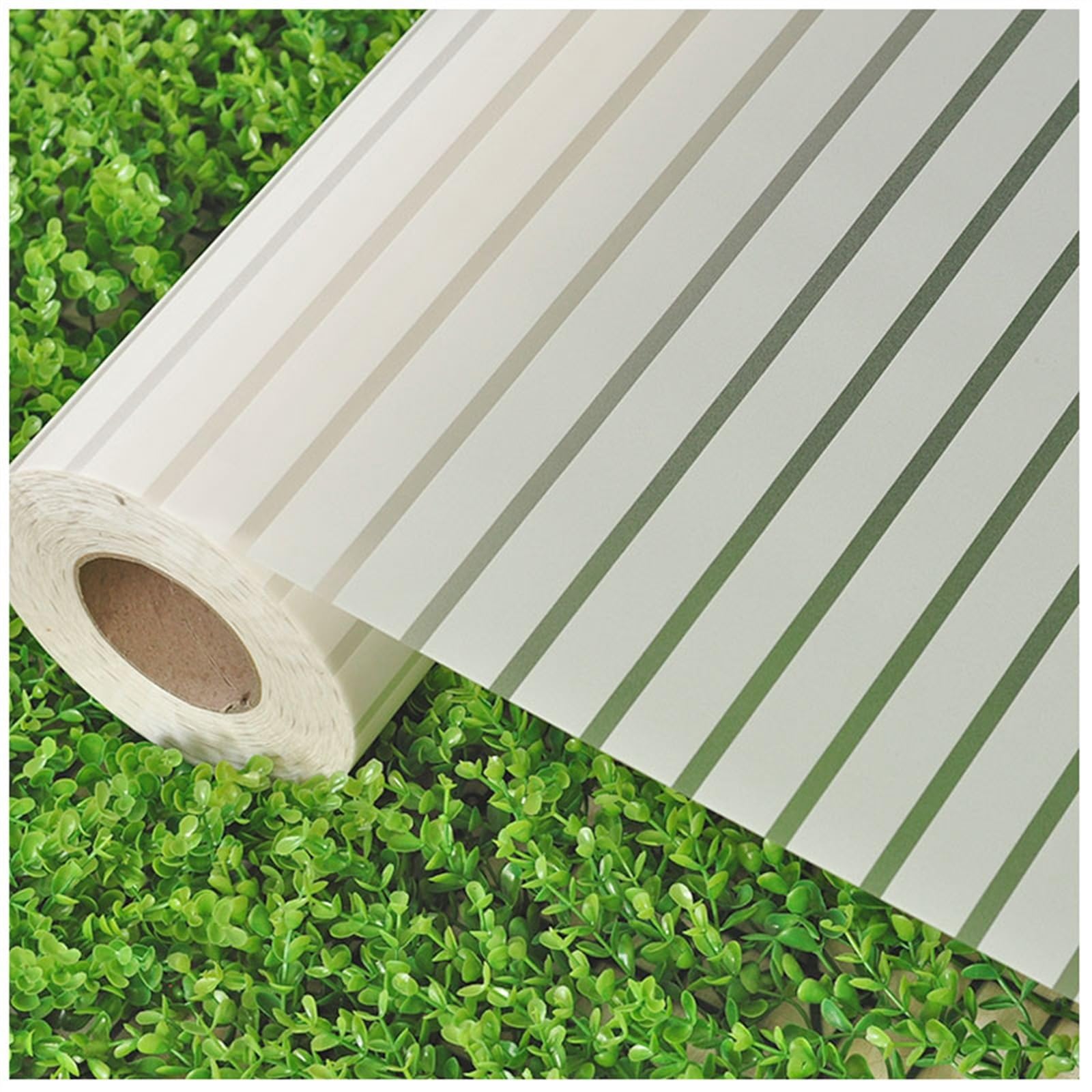 Một cuộn decal mờ cát có sọc trong suốt được cuộn một phần trên một lớp lá nhân tạo nhỏ, màu xanh lá cây tươi sáng.